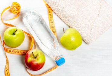 Water bottle, apples, measuring tape and towel on white wooden background. Top view